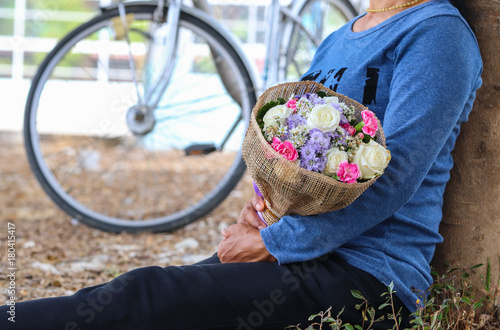 Asian girl waiting for boyfriend prepares a bouquet for him. Hold it in the embrace, That is love. May your Valentine's Day be filled. You are so special. Background blurred with bicycles.