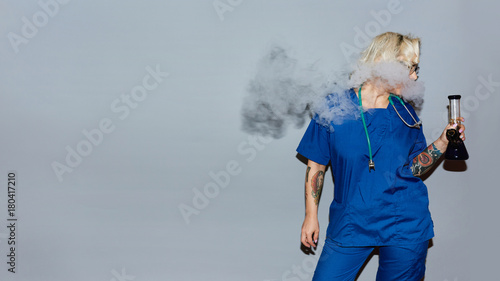 Nurse in blue uniform smoking bong against gray wall photo