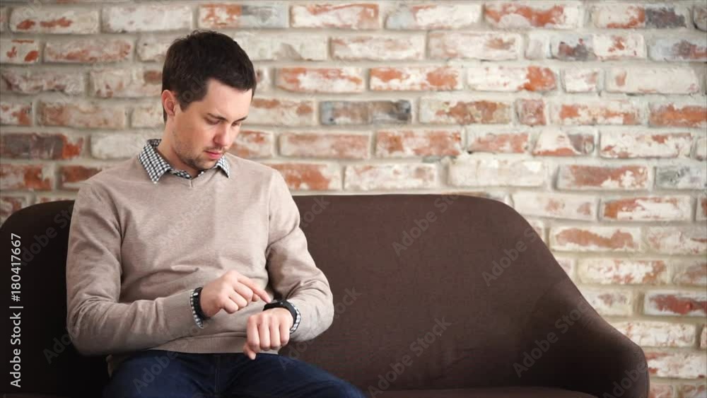 Young man sitting on the sofa in lobby and using smart watch while waiting Young man sitting on the sofa in lobby and using smart watch while waiting