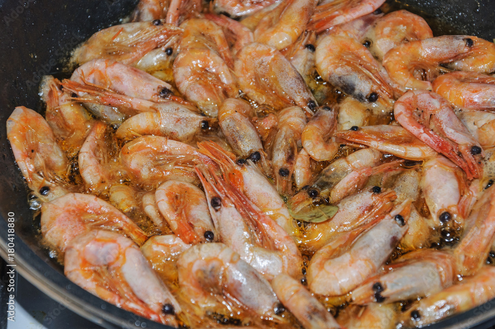 unpeeled shrimp fried in boiling olive oil in a frying pan