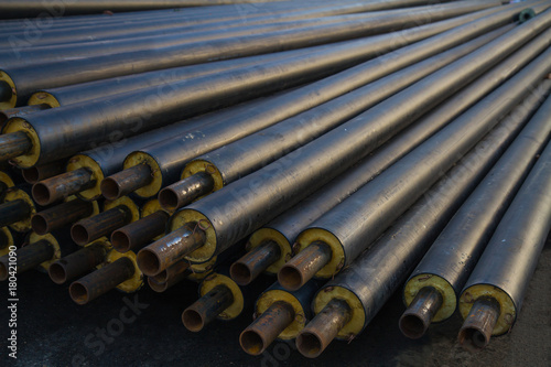black steel pipe with heat insulation on the construction site in a plastic tube wrapper lying on the pavement a bunch of horizontally. pipes for supplying gas or heat pressure medium