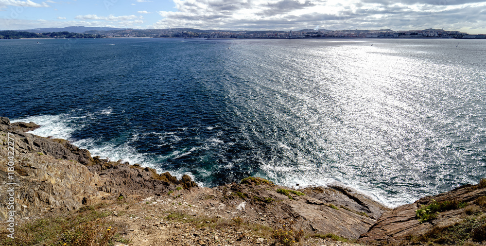 Obraz premium Panoramic view of the cliffs on the coast of Galicia (Spain). In the background the city of La Coruña. Sky with clouds with sun reflections