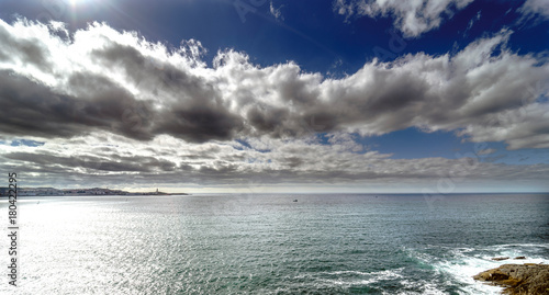 Fototapeta Naklejka Na Ścianę i Meble -  Panoramic view of the entrance of the bay of La Coruna on the coast of Galicia (Spain). Sky with clouds with reflections and sun facing
