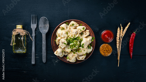 tasty homemade meat dumplings of wholemeal flour or russian pelmeni sprinkled with fresh parsley on plate on wooden table,copy space, view from above
