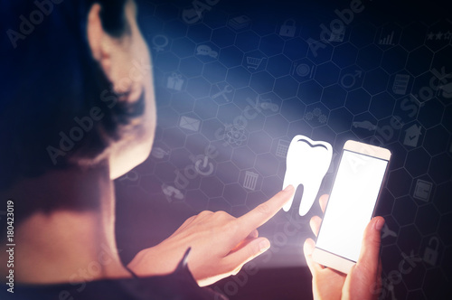 Image of a girl with a smartphone in hands. She presses on the tooth icon. Search for dentists, dental services, consultations.