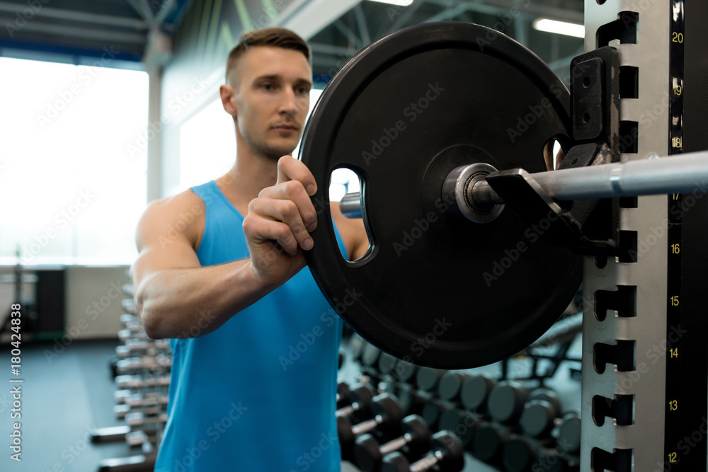 Portrait of handsome young man setting up barbell putting heavy plates on it during workout in modern gym Portrait of handsome young man setting up barbell putting heavy plates on it during workout in modern gym