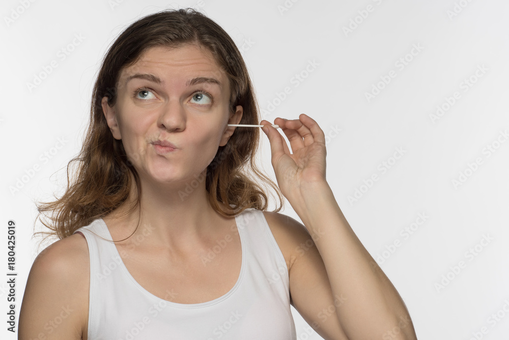 Young beautiful brunette girl cleans the ears with chopsticks with cotton wool and is surprised to get a lot of yellow earwax Young beautiful brunette girl cleans the ears with chopsticks with cotton wool and is surprised to get a lot of yellow earwax