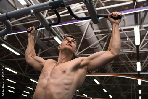 Low angle portrait of muscular young man with bare chest working out using machines in modern gym against background on metal ceiling