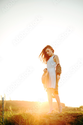Young girl in a white dress with a hat and a wonderful sunset