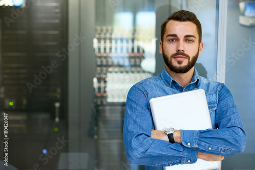 Leinwand Poster Portrait of beraded systems administrator posing holding laptop and looking at c