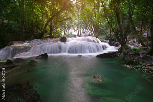 waterfall left side with clear green emerald water and rock for relax and refreshing cool with tree and root in the jungle or forest at Pha Tat waterfall for nature landscape background with sunlight © kornnphoto