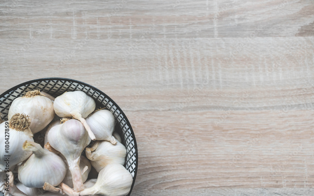 Top view of garlic in a black and white glass bowl on a wooden neutral background, top view Top view of garlic in a black and white glass bowl on a wooden neutral background, top view