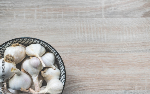 Top view of garlic in a black and white glass bowl on a wooden neutral background, top view