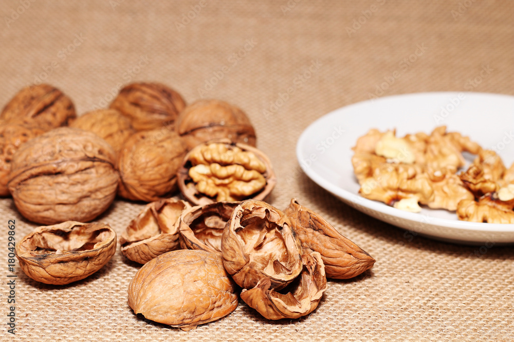 Opened and closed walnuts in a plate on a background of cloth and burlap Opened and closed walnuts in a plate on a background of cloth and burlap