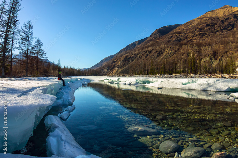 Girl sitting on the glacier ice melts in the spring on the river in the mountains