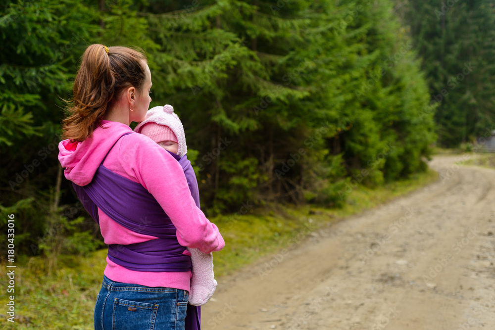 Mom with baby in sling for a walk in the woods Mom with baby in sling for a walk in the woods