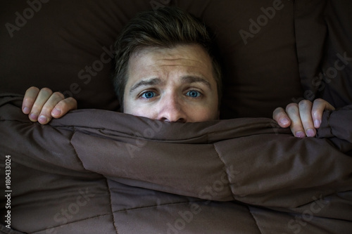 Caucasian young man hiding in bed under the blanket at home.