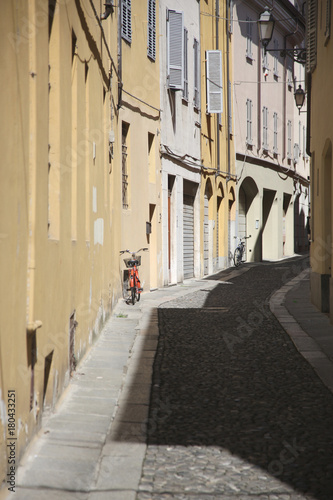 A red bicycle with a basket near the wall of the house on the small narrow street of the old town © Anna Jurkovska