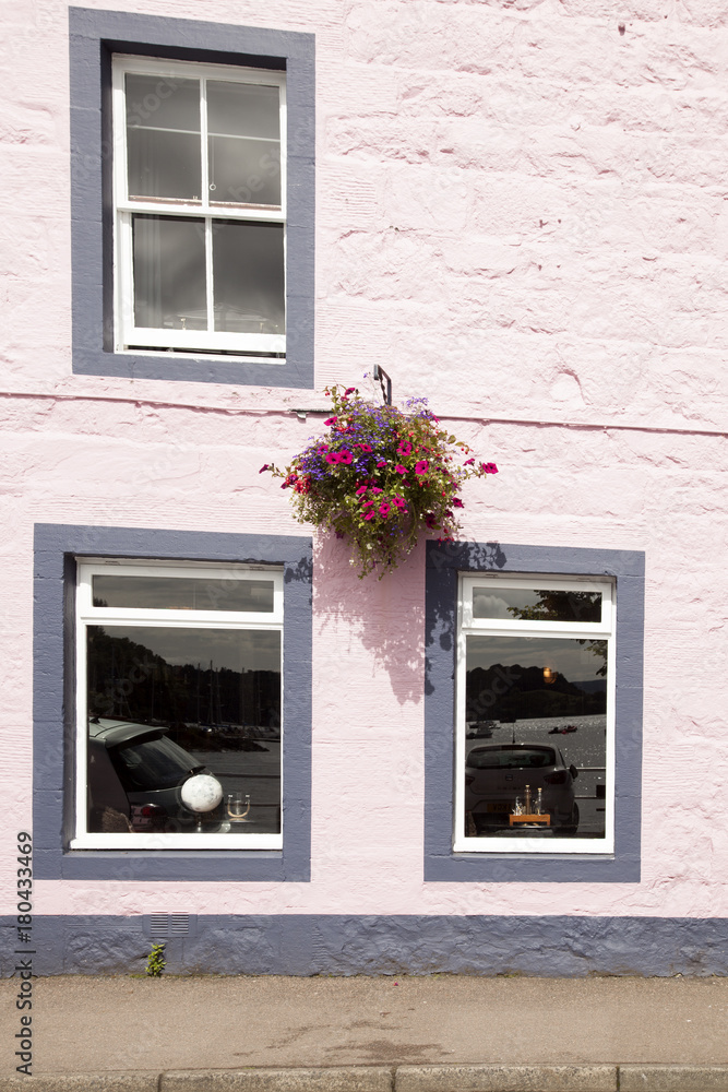 fachada pintada de rosa con tres ventanas blancas y una maceta colgada en el muro con flores colgado.