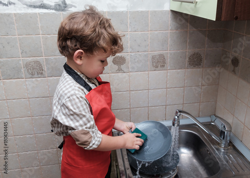 Fotografie European boy washes dishes at home