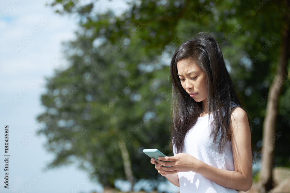 People, leisure, relaxation, rest, holidays and modern technologies concept. Beautiful serious young Asian woman messaging boyfriend online using electronic device during vacations in tropical country People, leisure, relaxation, rest, holidays and modern technologies concept. Beautiful serious young Asian woman messaging boyfriend online using electronic device during vacations in tropical country