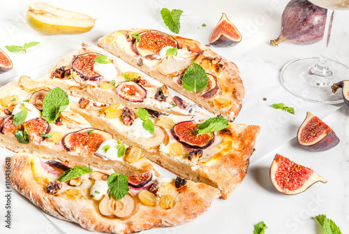 Autumn baking recipes. Sweet pie pizza or fruit focaccia with figs, pears, grapes, cream cheese, walnuts and mint. With white wine glass, on white marble background, copy space