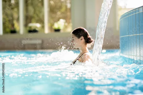Obraz Spokojna dziewczyna cieszy się strumieniem wodospadu i jego delikatnymi plamami w basenie w spa