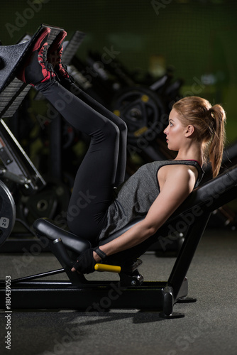 Sportive woman using weights press machine for legs at the gym. Pretty brunette exercising in a simulator. Working her quads at machine.