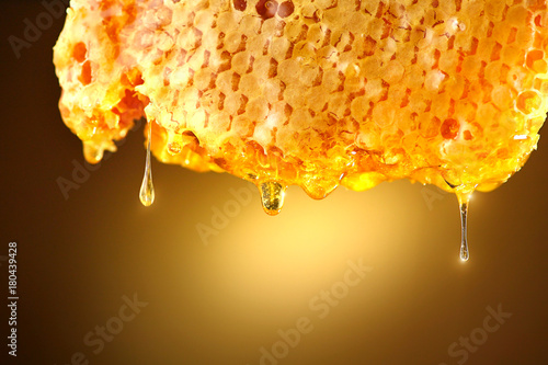фотографія Honey dripping from honey comb on yellow background. Thick honey