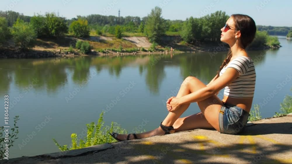Beautiful girl on the river bank. A teenage girl wearing sunglasses on the waterfront enjoys nature. Beautiful girl on the river bank. A teenage girl wearing sunglasses on the waterfront enjoys nature.