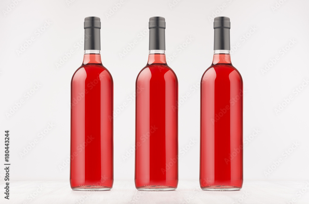 Three wine bottles with rose wine on white wooden board, mock up. Template for advertising, design, branding identity.