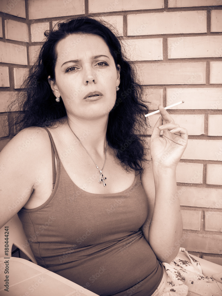 The harmful effect of nicotine on women's health and appearance. A middle-aged woman with a cigarette sits on the balcony and smokes. Harm from harmful habits The harmful effect of nicotine on women's health and appearance. A middle-aged woman with a cigarette sits on the balcony and smokes. Harm from harmful habits