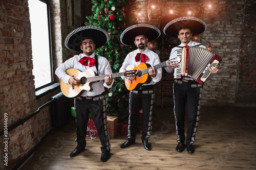 Mexican musicians mariachi near a Christmas tree.