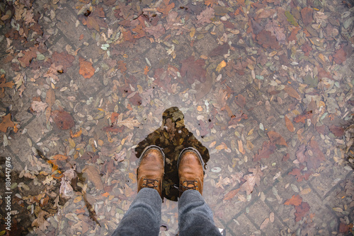 man in winter leather boots stands in a puddle with fallen leaves. © galaganov