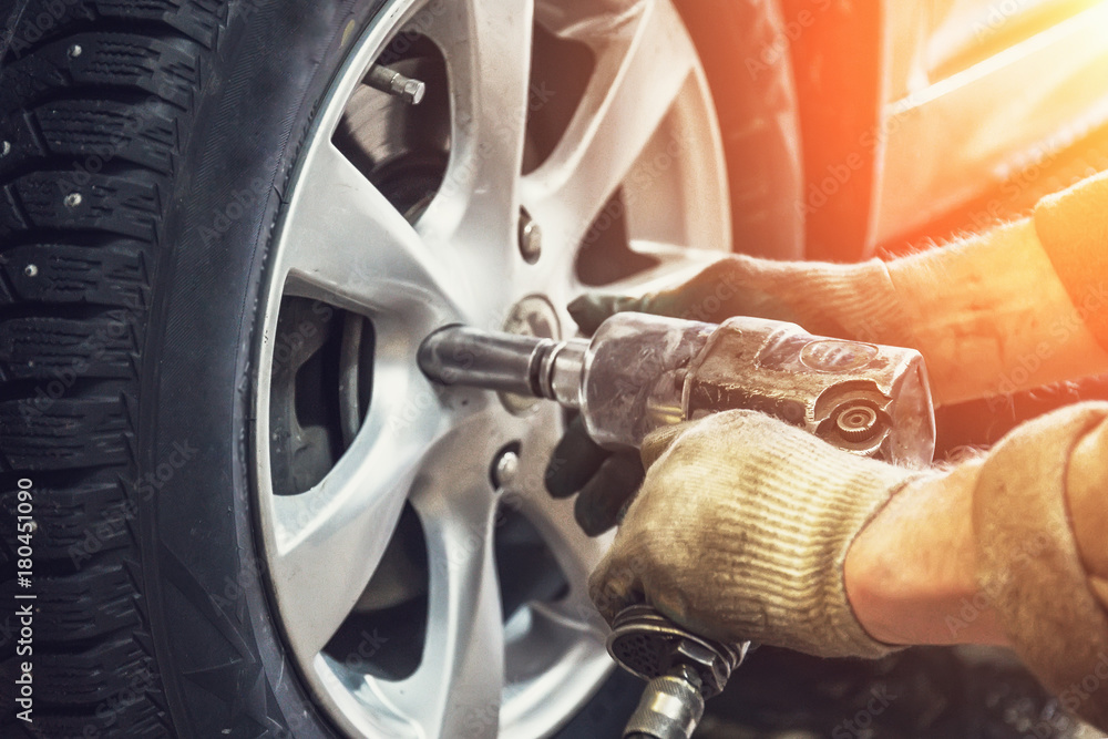 Naklejka premium Samochodowy mechanika pracownik robi oponie lub koła zastępstwu z pneumatycznym kluczem w garażu remontowa stacja obsługi
