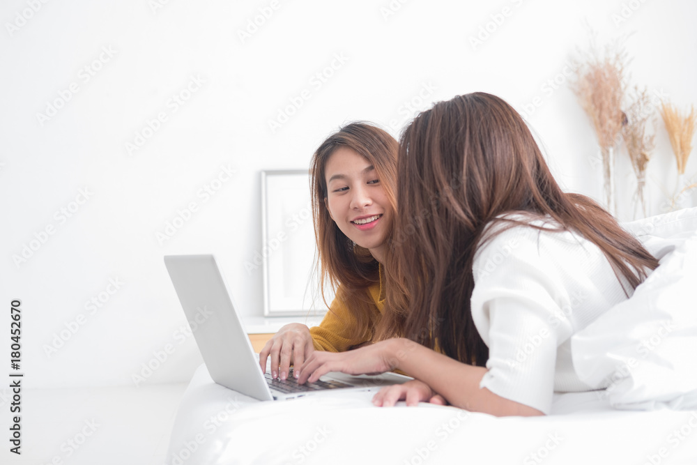 LGBT. Lovely lesbian couple together concept. Couple of young women using computer laptop on bed.