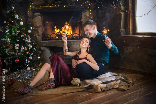 Joyful couple near christmas tree and fireplace with bengal lights selebrate New Year © illustrissima