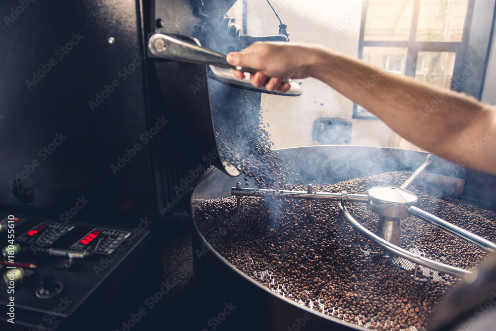 Man arm pressing button to open appliance. Coffee pouring from roaster machine to cooling cylinder. Industry concept. Close up