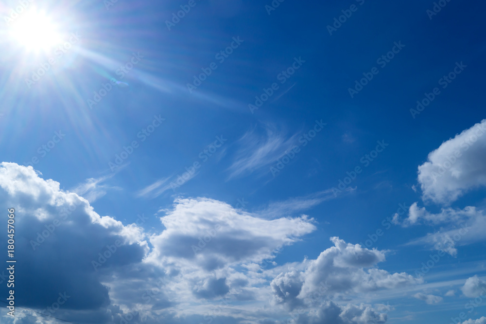 White cumulus clouds and sun on the blue sky
