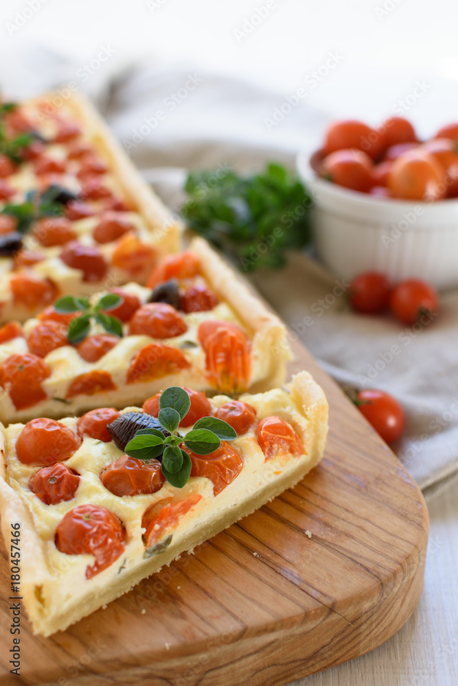 Rectangular tart with cherry tomatoes, ricotta, thyme, origan and black olives on rustic wooden cutting board on a linen cloth. Rustic style. Mediterranean cuisine. Rectangular tart with cherry tomatoes, ricotta, thyme, origan and black olives on rustic wooden cutting board on a linen cloth. Rustic style. Mediterranean cuisine.