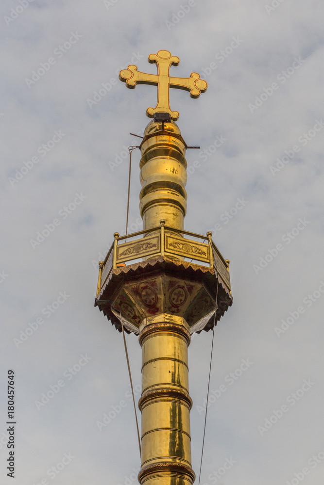 Narrow close up view of gold colored pillar with a cross at top