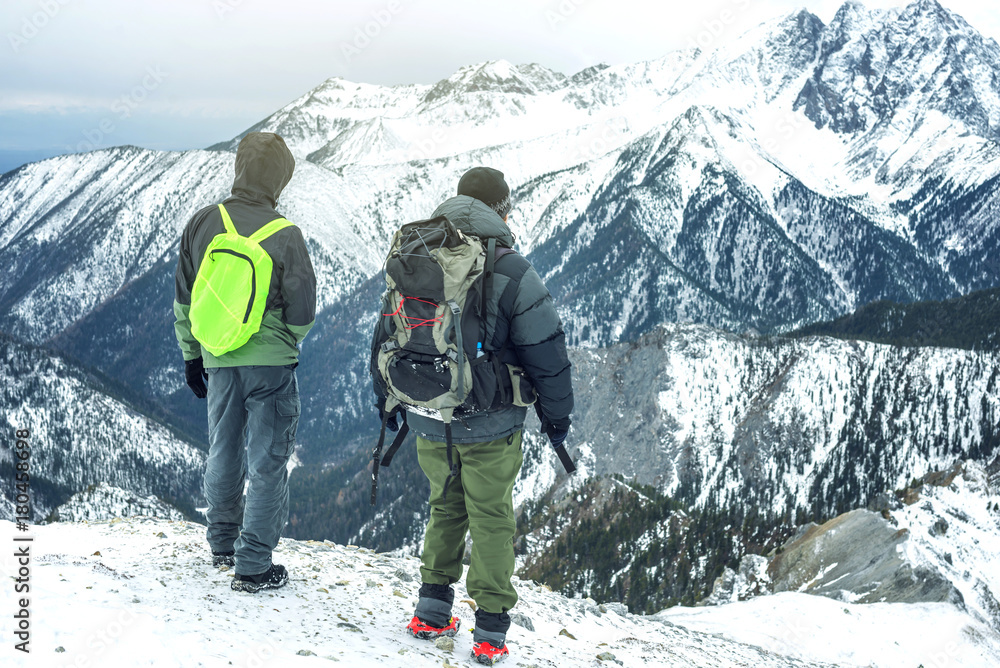 Men hikers with backpack on top of the mountain looking at the snow slope. Concept of motivation and goal achievement