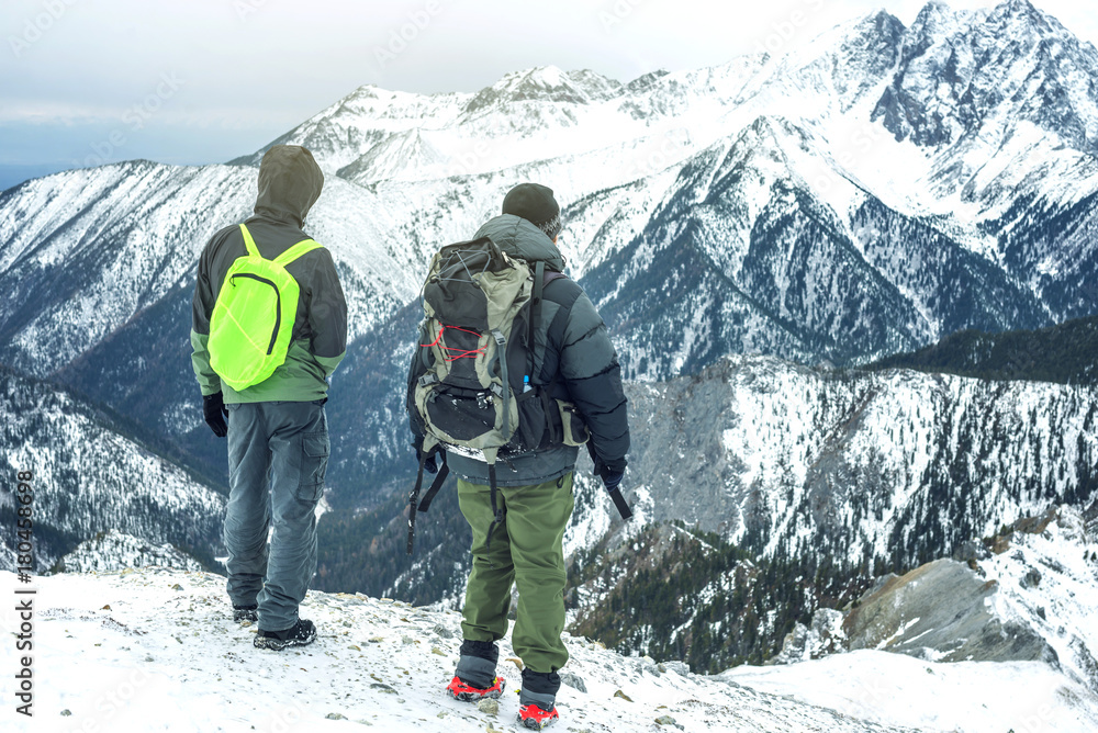 Men hikers with backpack on top of the mountain looking at the snow slope. Concept of motivation and goal achievement Men hikers with backpack on top of the mountain looking at the snow slope. Concept of motivation and goal achievement