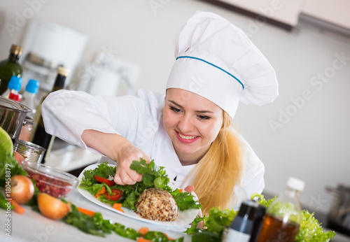 Female cook arranging herbs decoration on plate with salad