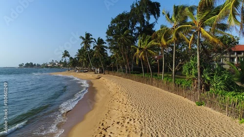 Aerial of sea waves, sandy beach and holiday houses behind the wooden fence in Sri Lanka