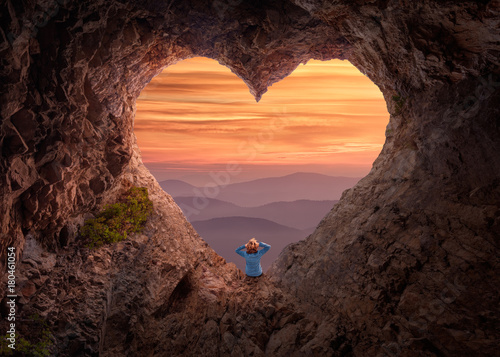 Woman in heart shape cave towards the vast landscape