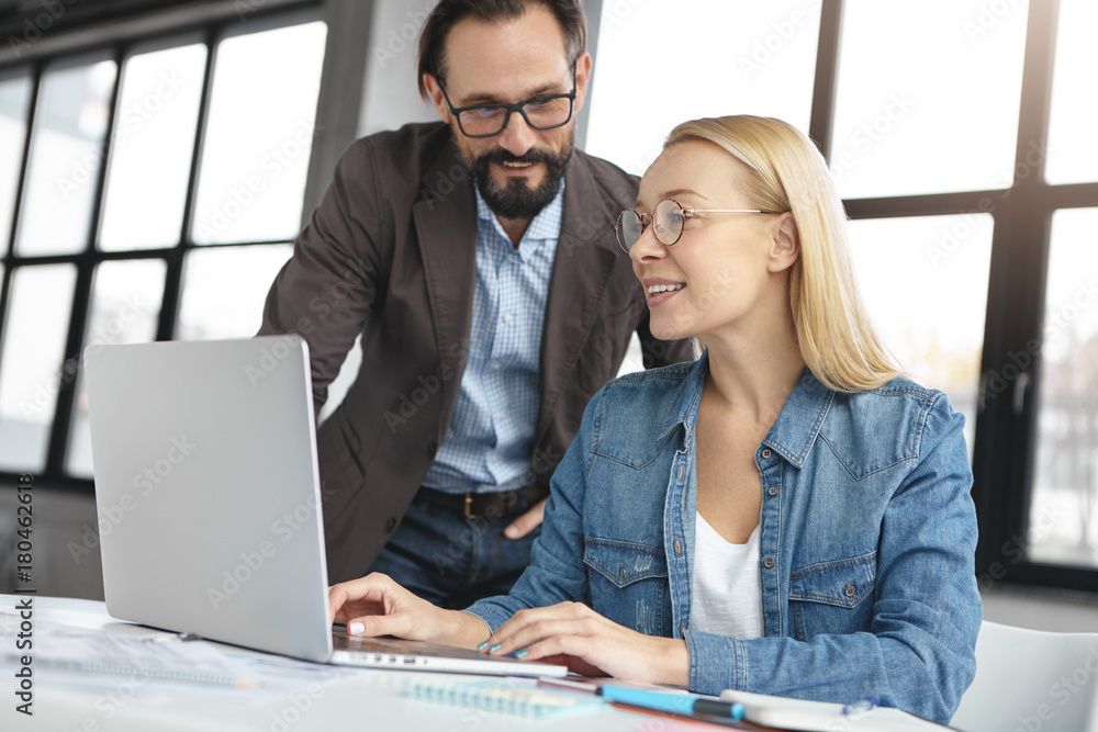 Young female inspector and bearded administrator businessman look attentively into screen of laptop, discuss data together, analyze financial figures, denote progress of company. Audit concept Young female inspector and bearded administrator businessman look attentively into screen of laptop, discuss data together, analyze financial figures, denote progress of company. Audit concept