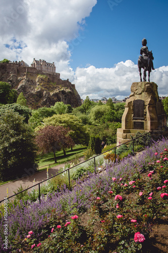 Princes street gardens and the statue of Thomas Guthrie with Edinburgh Castle visible in the background on a beautiful sunny day