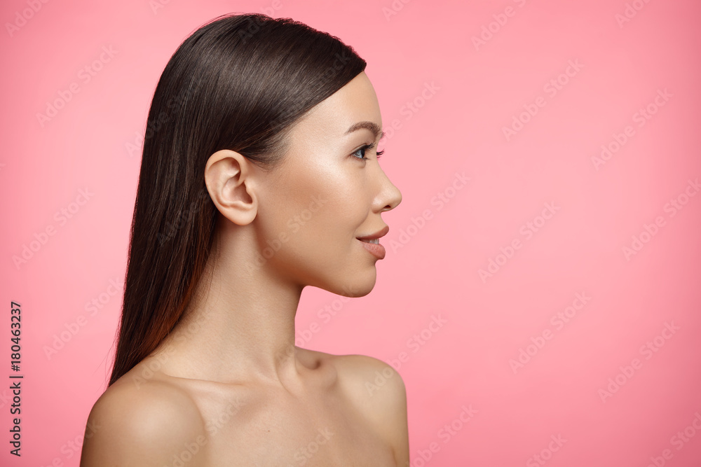 Sideways portrait of naked brunette young female with healthy skin, looks aside, isolated on pink background. Woman wears no clothes. Beauty, health concept. Adorable girl poses in studio. Feminity Sideways portrait of naked brunette young female with healthy skin, looks aside, isolated on pink background. Woman wears no clothes. Beauty, health concept. Adorable girl poses in studio. Feminity