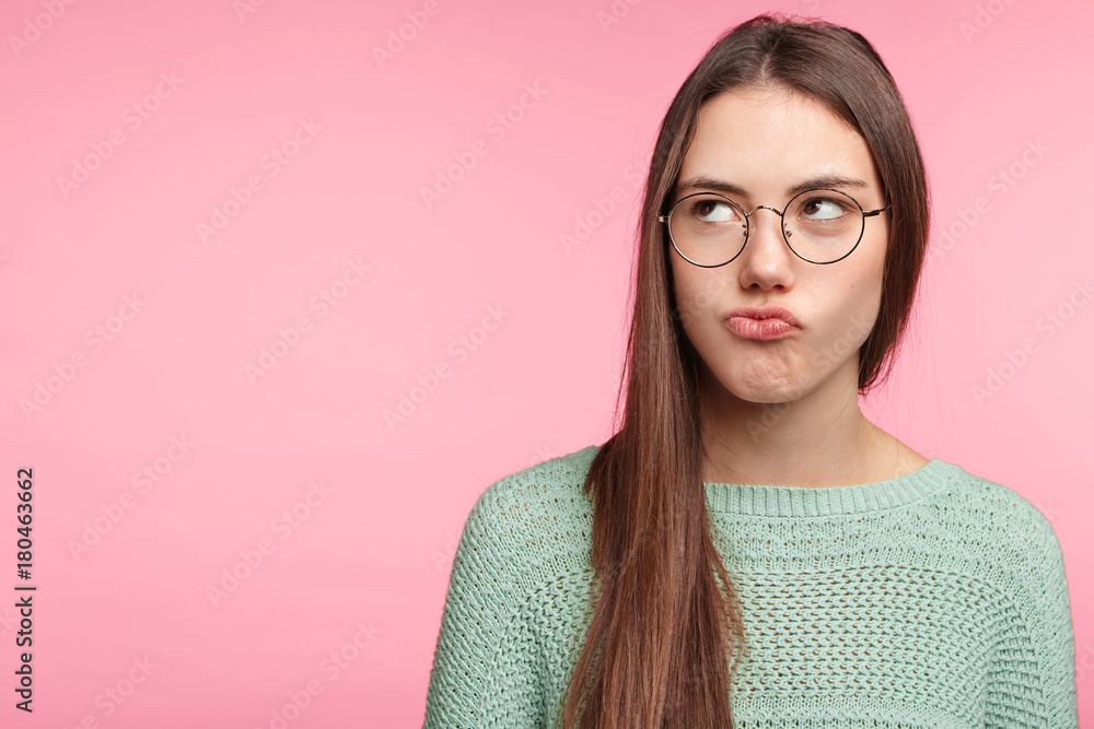Fototapeta premium Horizontal portrait of displeased offended female pouts lips, being abused by boyfriend, has bad relationships, looks aside with discontent expression, frowns face. Facial expressions concept